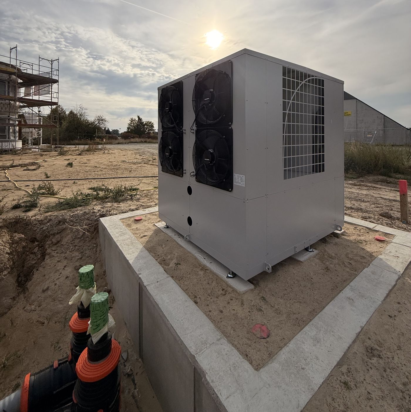 Wärmepumpe auf Betonfundament, im Vordergrund die Rohrdurchführungen der erdverlegten Trasse